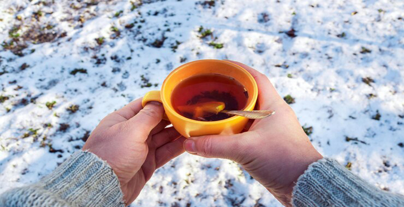 فنجان چای یا دمنوش در دست در کنار برف ها